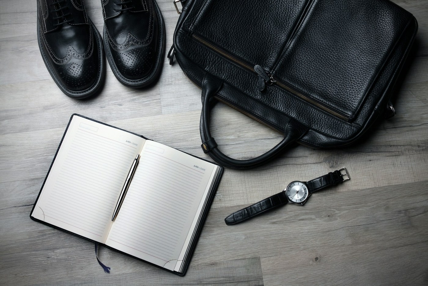 Black bag, shoes, notebook and wristwatch on a wood surface; stock photography for a fictional demo
